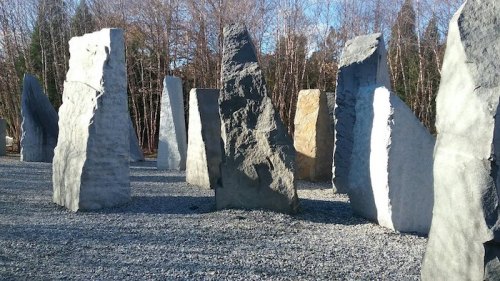 A circle of large, uneven stone monoliths surrounded by gravel and trees in a natural setting.
