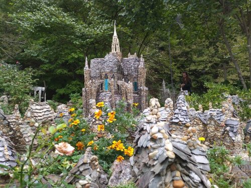 A whimsical stone castle surrounded by colorful flowers and miniature buildings in a lush garden setting.