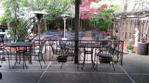 A cozy outdoor patio with metal chairs and tables, surrounded by greenery and decorative plants.
