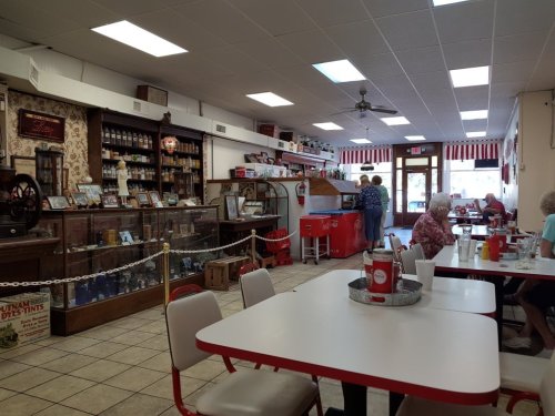 A cozy diner interior with vintage decor, tables, and patrons enjoying their meals. A display case and ice cream freezer are visible.