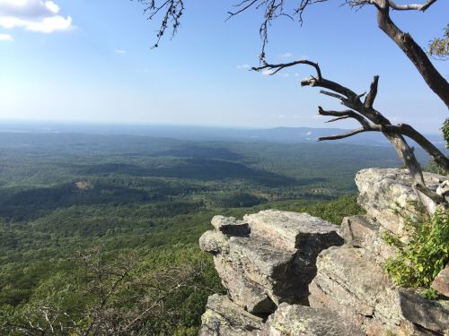 A panoramic view of lush green mountains and valleys under a clear blue sky, with rocky outcrops in the foreground.