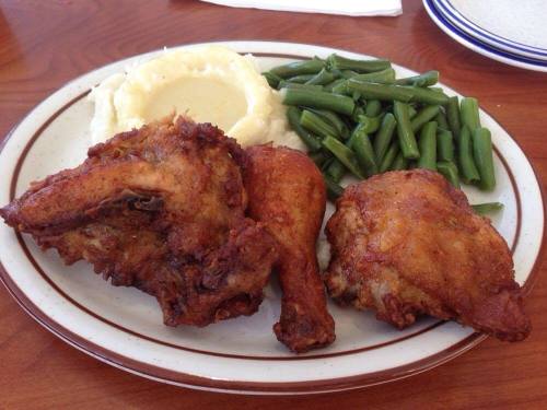 A plate of fried chicken with mashed potatoes and green beans on a wooden table.