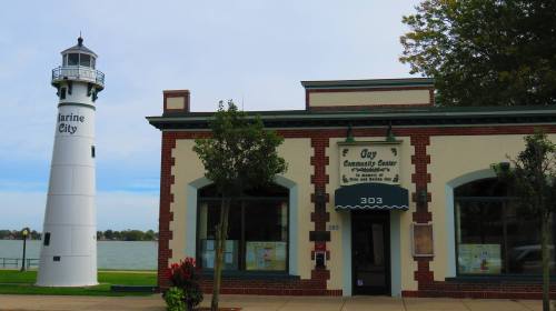 A lighthouse next to a brick building with a sign for the Guy Community Center, overlooking a body of water.