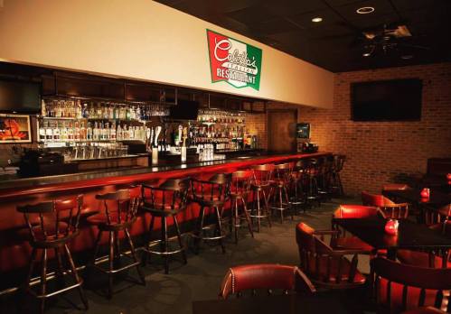 A cozy bar area with wooden stools, a well-stocked counter, and soft lighting in a restaurant setting.