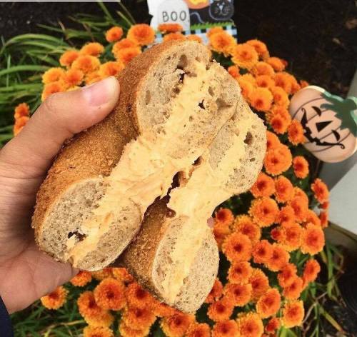 A hand holding a sandwich with peanut butter and jelly, surrounded by vibrant orange flowers and a Halloween decoration.