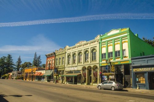 Colorful historic buildings line a quiet street under a clear blue sky with wispy clouds.