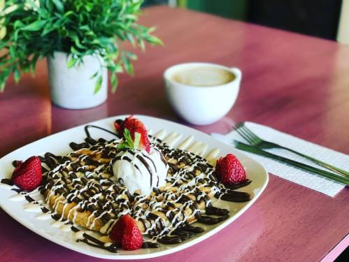 A plate of waffles topped with ice cream, chocolate drizzle, and strawberries, with a coffee cup in the background.