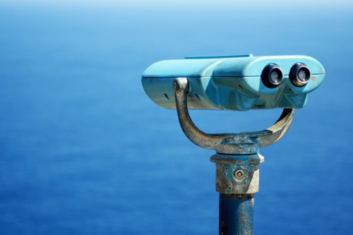 A blue binocular viewer mounted on a pole, overlooking a calm blue ocean.