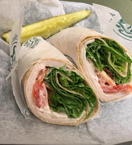 A close-up of a sliced wrap filled with turkey, lettuce, and tomato, served with a pickle on the side.