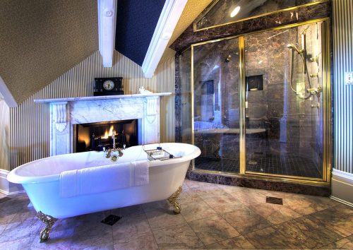 Luxurious bathroom featuring a freestanding tub, marble fireplace, and a glass shower in an elegant setting.