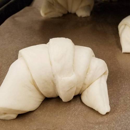 Raw, unbaked croissant dough shaped and resting on parchment paper.