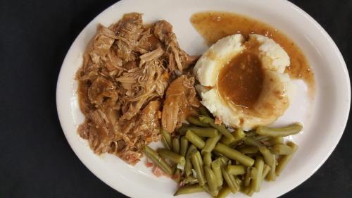 A plate with pulled pork, mashed potatoes with gravy, and green beans on a black background.