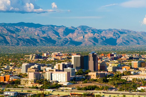 A panoramic view of a city skyline with mountains in the background under a clear blue sky.