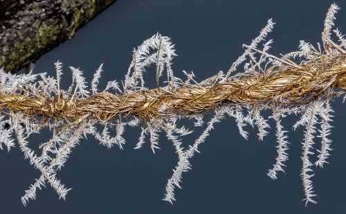 A close-up of a twisted golden rope adorned with frost, set against a dark blue background.