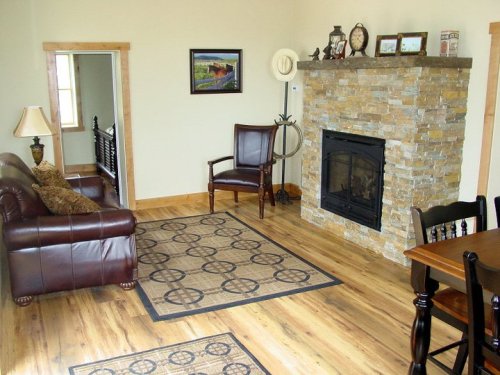 Cozy living room with a stone fireplace, leather sofa, wooden dining table, and warm wooden floors.