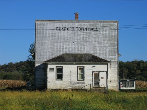 A weathered building labeled "Elkport Town Hall," surrounded by tall grass and a clear blue sky.