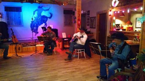 A cozy indoor scene with musicians playing guitars, decorated with warm lights and a blue horse mural on the wall.