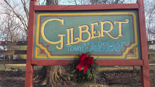 Sign for Gilbert, Arkansas, reading "Gilbert: The Coolest Town in Arkansas," decorated with a red bow and greenery.