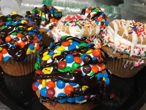 Colorful cupcakes topped with chocolate drizzle, sprinkles, and candy-coated chocolates on a black plate.