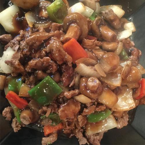 A close-up of a bowl filled with beef stir-fry, featuring mushrooms, bell peppers, and onions in a savory sauce.