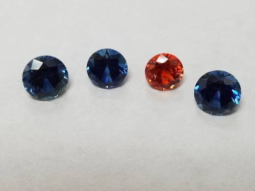 Four round gemstones in varying shades: two blue, one orange, and one deep blue, displayed on a light background.