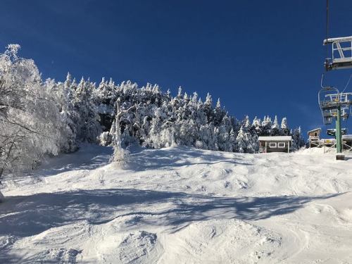 Snow-covered slope with a ski lift and frosted trees under a clear blue sky.