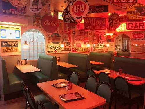 Retro diner interior with green booths, wooden tables, and vintage advertisements on the walls, illuminated by warm lights.