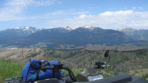 A scenic view of mountains and valleys, with an ATV and a blue bag in the foreground under a clear sky.