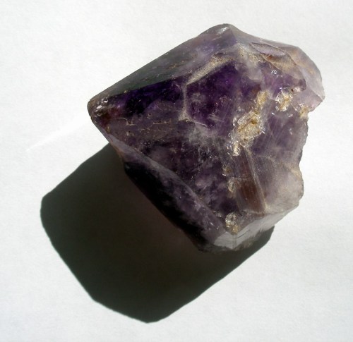 A rough amethyst crystal with deep purple hues and a light shadow on a white background.