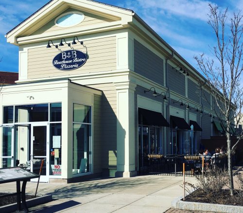 Exterior of a pizzeria with a sign reading "B&B Bourbon Bistro Pizzeria," featuring outdoor seating and a clear blue sky.