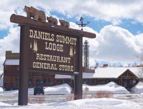 Sign for Daniels Summit Lodge with carved bears, surrounded by snow and a rustic building in the background.