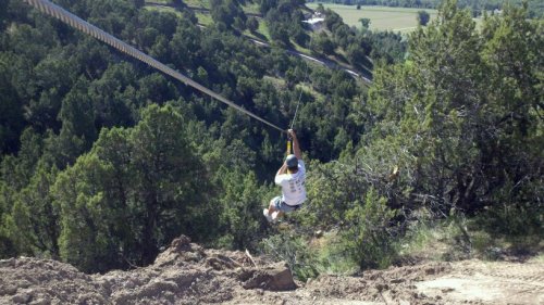 A person zip-lining over a lush green landscape with trees and hills in the background.