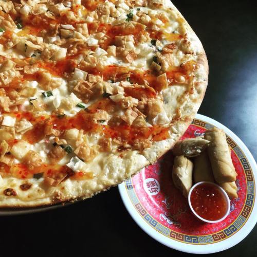 A large pizza topped with crispy pieces and drizzled with sauce, alongside a plate of spring rolls and dipping sauce.
