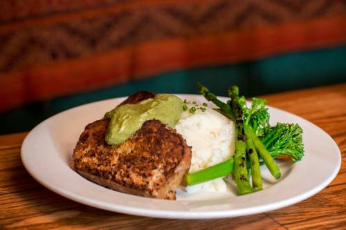 A plate featuring a breaded fish fillet topped with green sauce, served with mashed potatoes and grilled asparagus.