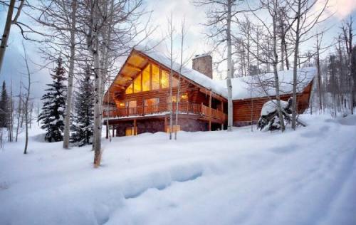 A cozy wooden cabin surrounded by snow-covered trees, with warm lights glowing from its windows.
