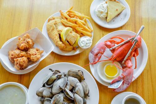 A spread of seafood dishes including fried fish, lobster, clams, hushpuppies, fries, and a slice of pie on a wooden table.