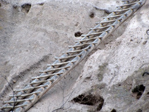 A wooden ladder rests against a rocky, textured surface, with small holes visible in the stone.