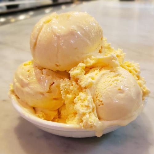 A bowl of three scoops of creamy yellow ice cream, with some melting and a smooth texture.