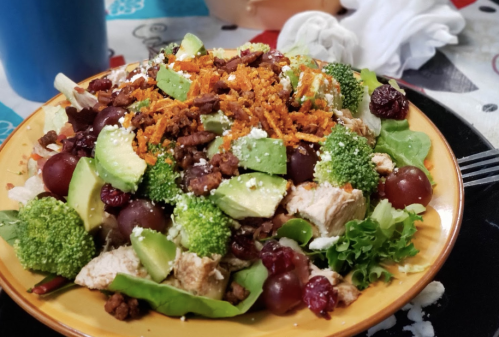 A colorful salad with chicken, avocado, grapes, broccoli, carrots, and cranberries on a plate.