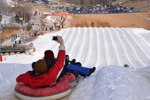 A group of people on snow tubes at the top of a snowy hill, preparing to slide down a slope.