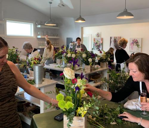 A group of people arranging flowers in a bright, modern workshop with various floral arrangements and supplies.