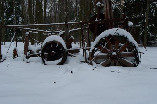 Snow-covered vintage farm equipment partially buried in a winter landscape, surrounded by trees.