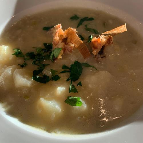 A bowl of creamy soup with diced potatoes, garnished with herbs and crispy toppings.