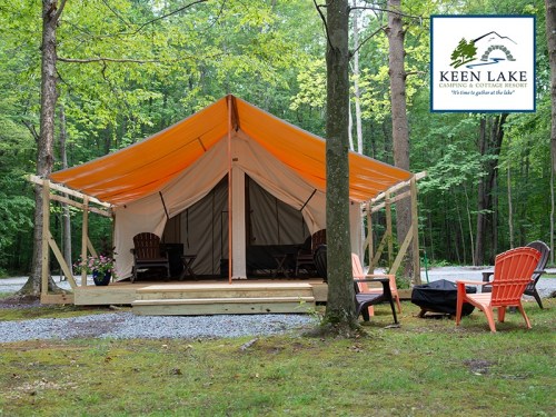A spacious tent at Keen Lake Camping Resort, surrounded by trees and featuring outdoor seating.