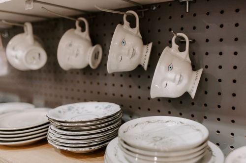 A shelf displaying decorative plates and unique face-shaped mugs hanging on a pegboard.