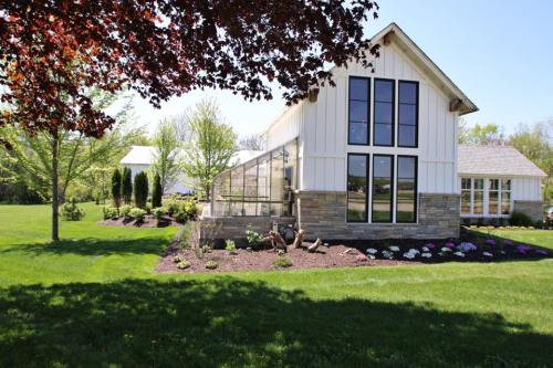 A modern house with large windows, surrounded by lush green grass and colorful flower beds under a clear blue sky.