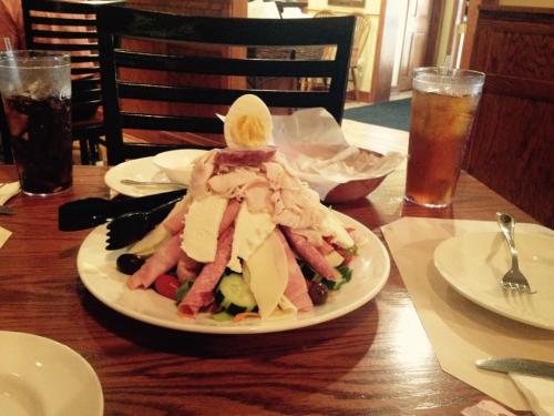 A large salad topped with various meats, cheeses, and a halved egg, served on a white plate at a restaurant table.