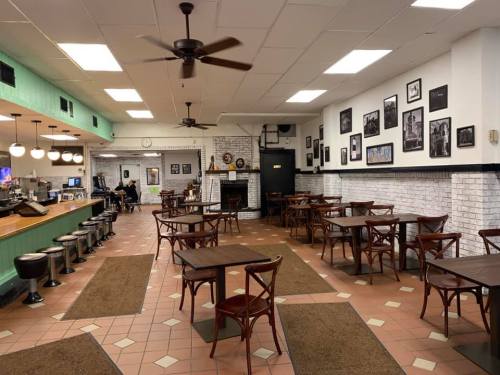 A cozy café interior with wooden tables, chairs, and a brick wall adorned with black-and-white photos.