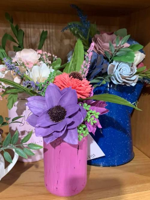 Colorful artificial flowers in pink and blue vases, displayed on a wooden shelf.