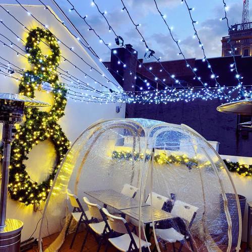 A cozy outdoor dining area with string lights, a clear dome, and festive decorations on a rooftop.